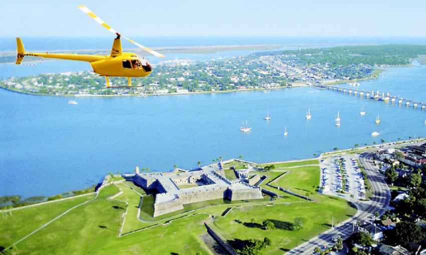 The bright yellow First City Helicopter, flying high over the Castillo and bayfront during a tourist flight