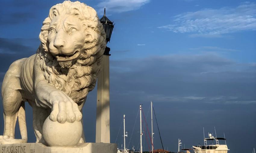 One of the two lions on the city side of the Bridge of Lions, boats in the mooring field in the background