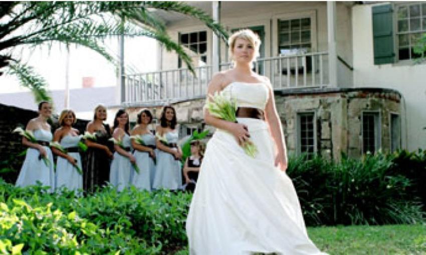 A bride in a strapless dess with wide black satin ribon at the waist, with her bridesmaids in the background, at the Oldest House in St. Augustine