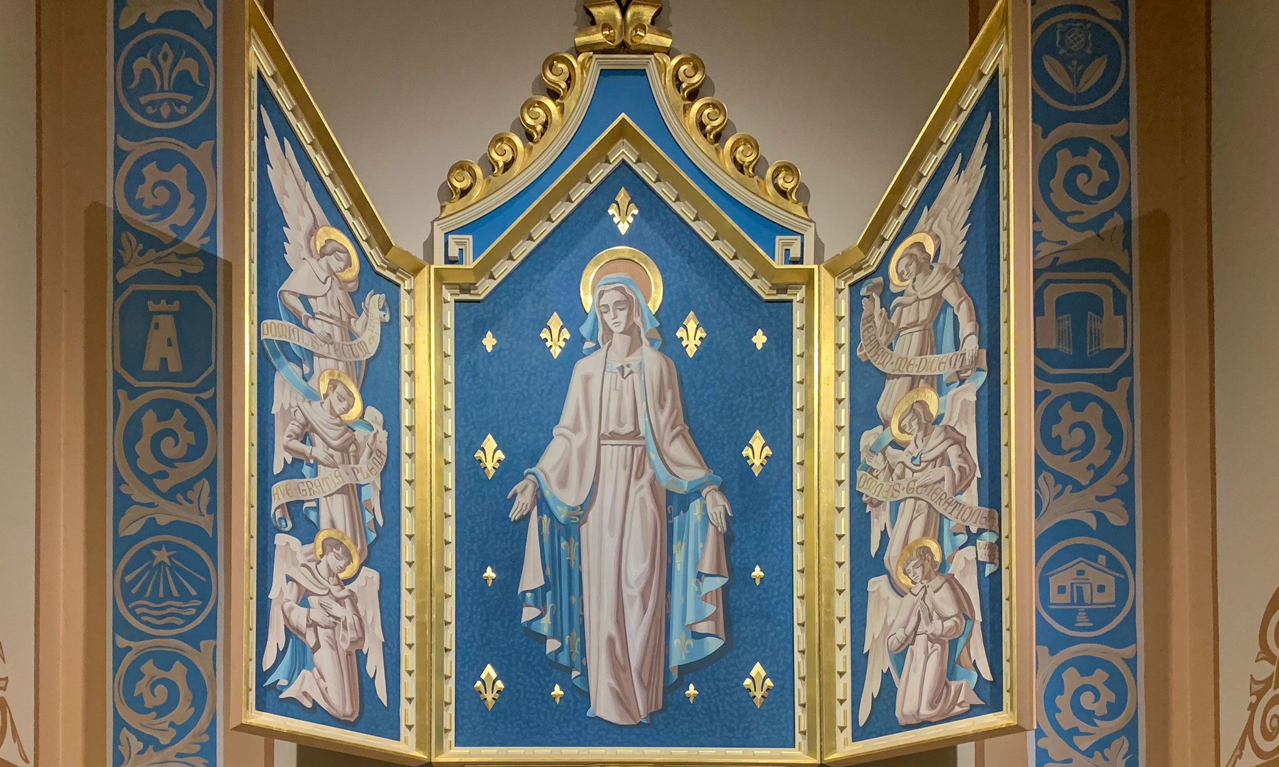 The triptych by Hugo Ohlms which honors and celebrates the Virgin Mary in the Cathedral Basilica of Saint Augustine in St. Augustine, Florida. Painted with royal blue and shining gold leafing, Mary occupies the center whilst angels flank her on either side. Saint Augustine, Florida is also the location of the first Marian shrine in the United States.