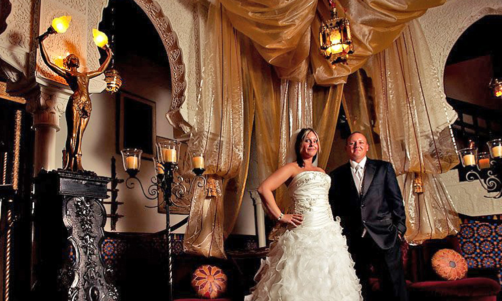 A bride in a frothy white dress standing with her groom in the ornate Villa Zorayda parlor