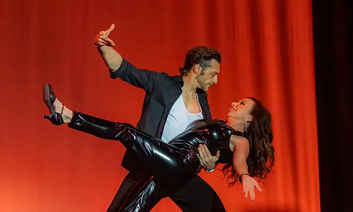 Two dancers in black, during a dramatic number, with the woman leaning back in the man's arm
